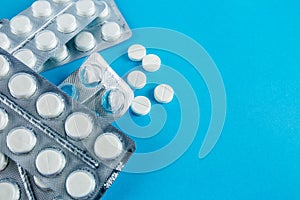 White round pills in pack. Tablets are next to the packaging on a blue background