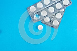 White round pills in pack. Tablets are next to the packaging on a blue background