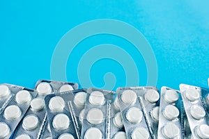 White round pills in pack. Tablets are next to the packaging on a blue background