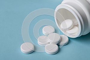 White round pills pouring out of the medicine bottle on blue background with copy space