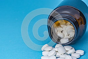 White round pills scattered from a brown bottle on a blue background. Pharmacy and healthcare theme.