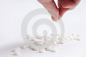 White round pills in on a white background. A hand holding one small round med.