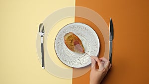 White round plate, knife with fork on brown background, female hand puts dry yellow leaf into plate
