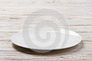 White Round Plate on white wooden table background. Perspective view