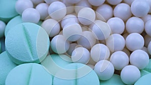 White round small granules lie among green pills and rotate closeup