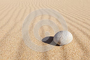 White round stone lying on clean sand. Concept of balance, harmony and meditation. Minimalism