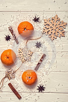 White rustic table with tangerines, cinnamon sticks, anise-star, wooden snowflakes, artificial snow. Vertical Christmas background