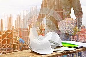 White safety helmet and paper plan blueprint on wood floor table with concept Double Exposure engineering in working building