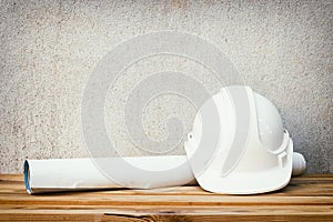 white safety helmet plastic and paper roll plan blueprint construction of engineering on wood floor table background