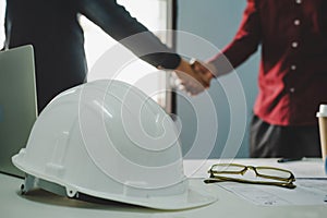 White safety helmet on workplace desk with construction worker team hands shaking