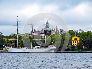 White sailboat on the background of green trees and beautiful buildings of Stockholm Sweden