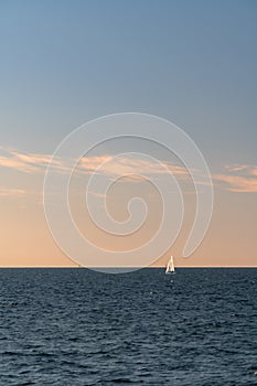 White sailboat on a calm sea or ocean during sunset