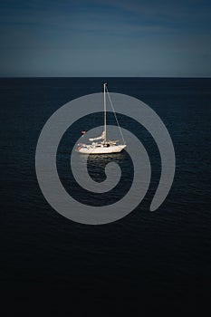 White sailboat in a deep blue ocean surrounded by clear blue skies