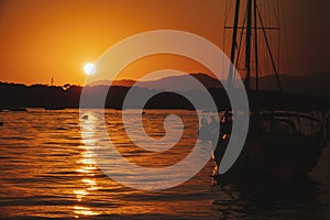 A white sailboat sails on the sea with an orange sunset