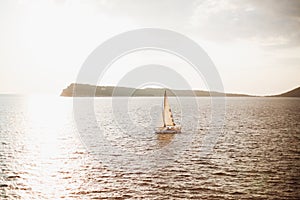 White sailing ship sails on the sea against the background of the mountain. The sun shines brightly