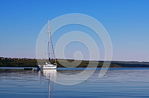 White sailing yacht stands anchored against the backdrop of the picturesque shore in the foreground water in full calm