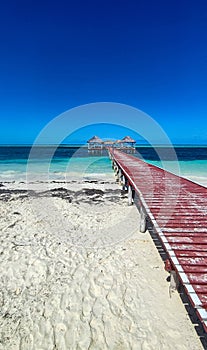 White sand beach, Atlantic Ocean with wooden pier and huts on a sunny day. Tropical seascape photography in horizontal