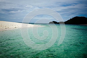 White sand beach on lonely island in tropical sea, light blue green sea, blue sky with white clouds photo