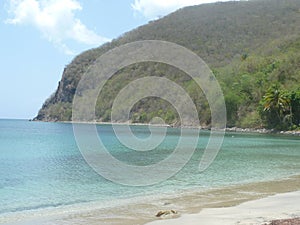 A white sand beach, the paradise sea and behind a forested hill