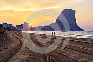 White sand beach at sunset with a couple of people walking along the shore. Calpe alicante.