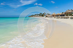 White sand beach and turquoise water  ocean on green palm trees and blue sky background. Aruba.