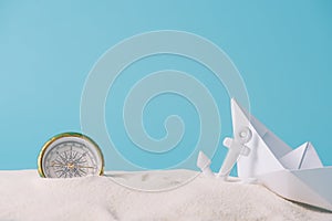 White sand with paper boat, compass and anchor