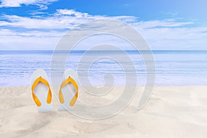 White sandal flip flop on sand beach with beautiful seascape view of sea and blue sky in the background.