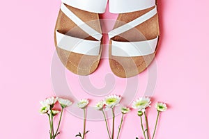 The white sandals and flowers on pink background top view.