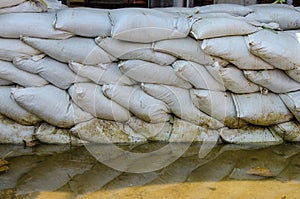 White sandbags for flood defense and it's reflection brown water