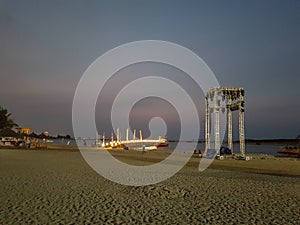 white sandy beachside view in the evening with bridge lights and stage performances