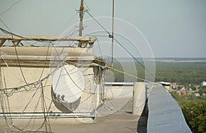 White satellite dish with three converters mounted on residental building rooftop concrete wall. Satellite television