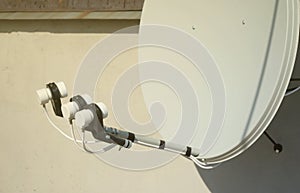 White satellite dish with three converters mounted on residental building rooftop concrete wall. Satellite television