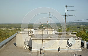 White satellite dish with three converters mounted on residental building rooftop concrete wall. Satellite television