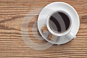 White saucer and cup of coffee with two cane sugar pieces on rustic wooden table background top view have place for text