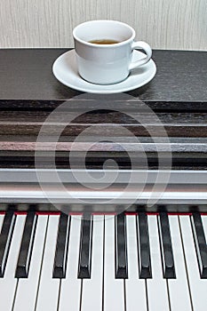 A white saucer and a cup of tea on the brawn opened piano.