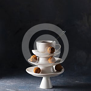 White saucer pyramid with cup of tea with spoon on top decorated with chocolate truffles on empty background. Creative concept,