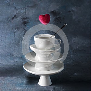 White saucer pyramid with cup of tea on top and flying red hearts candy over it. Dark background. Creative concept, love,