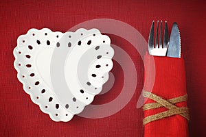 White saucer in the shape of a heart on a red background with cutlery in a napkin