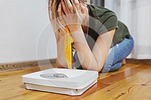 White scale and depression, upset and sad woman with measuring tape on wooden floor