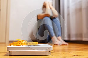 White scale and upset and sad woman with measuring tape on floor