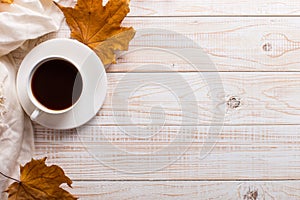 White scarf, cup of coffee and dry yellow leaves on a wooden table. Autumn mood, copy space