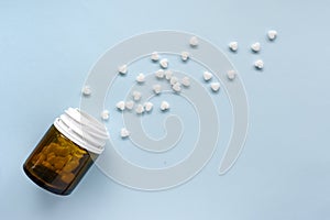 White scattered pills in the shape of a heart and a jar with dark glass on a blue background