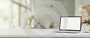 A white screen laptop computer on a white desk in a contemporary bright coffee shop