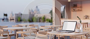 A white screen laptop mockup on a table in a modern and contemporary co-working space or coffee shop