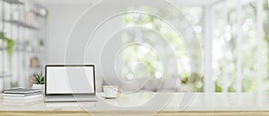 A white-screen laptop mockup on a white tabletop over a blurred, modern bright living room