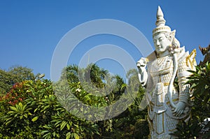 White sculpture of Spirit Nat guard surrounded by tropical trees at Kyauktawgyi Pagoda complex in Mandalay photo