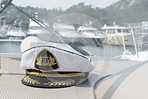 White sea captain`s cap on the dashboard of the boat, the boats are parked in the background