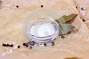 White sea salt in glass bowl with spices on light beige parchment paper textured background.