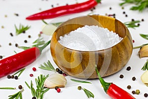 White sea salt in a round wooden bowl with red chilli pepper, peppercorns, garlic and rosemary on food background.