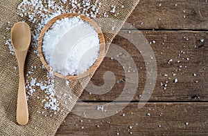 White sea salt in wood bowl with wood spoon on gunny sack cloth on brown wooden table